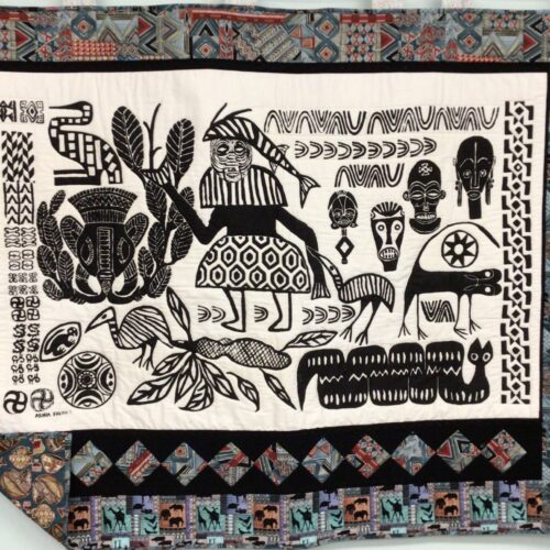 Wall hanging featuring African Ashia batik panel in black and white with tribal masks, animals, and geometric designs bordered with pieced blocks