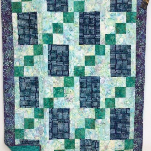 Handmade lap quilt featuring a geometric mosaic of blue and green batik fabrics with a coordinating batik backing.