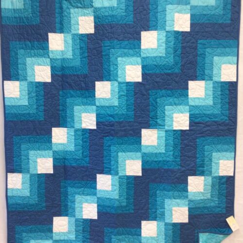 Throw quilt with quarter log cabin blocks in shades of blue with white centers and loopy long arm quilting