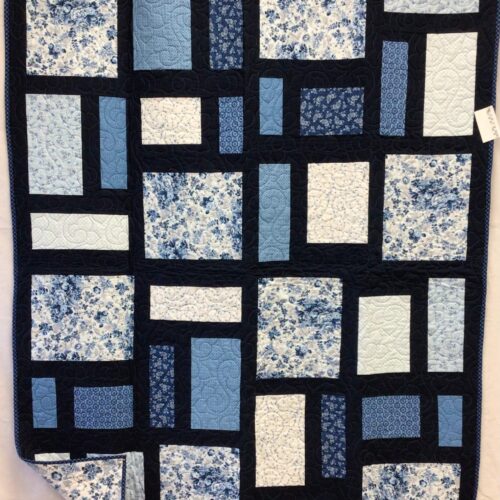 Modern throw quilt with asymmetric rectangular blocks in blue florals, solids, and creams against black sashing