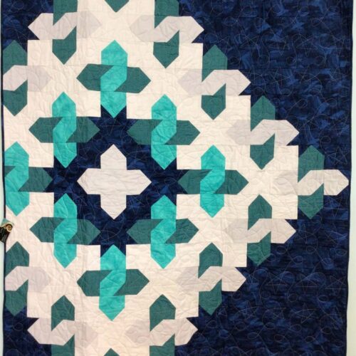 Throw quilt with large geometric star cosmic cloud pattern with teal shades on navy blue background with star and loop quilting motif