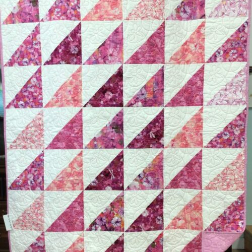 Throw quilt with half square triangles in white and various pink and purple dragonfly and floral prints with dragonfly quilting
