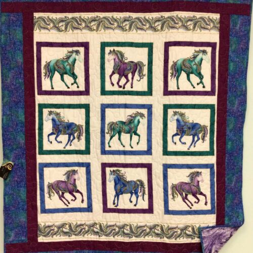 Panel quilt featuring nine carousel horses in jewel tones of teal, purple, and blue with ornate decorations, framed with multiple borders