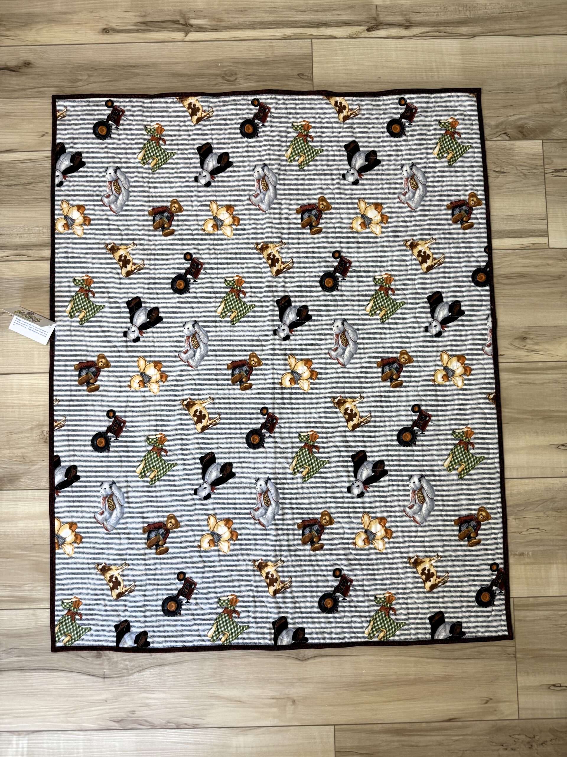Baby quilt with toy teddy bears, farm animals, dogs, and pandas scattered across gray and white horizontal striped background