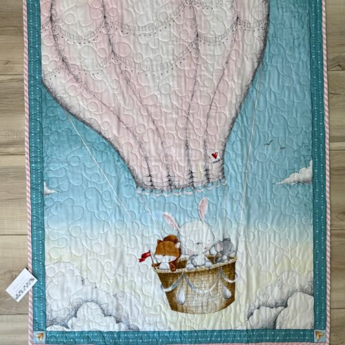 Baby quilt featuring bunny and friends in cream hot air balloon on soft blue sky background with teal borders and long arm quilting