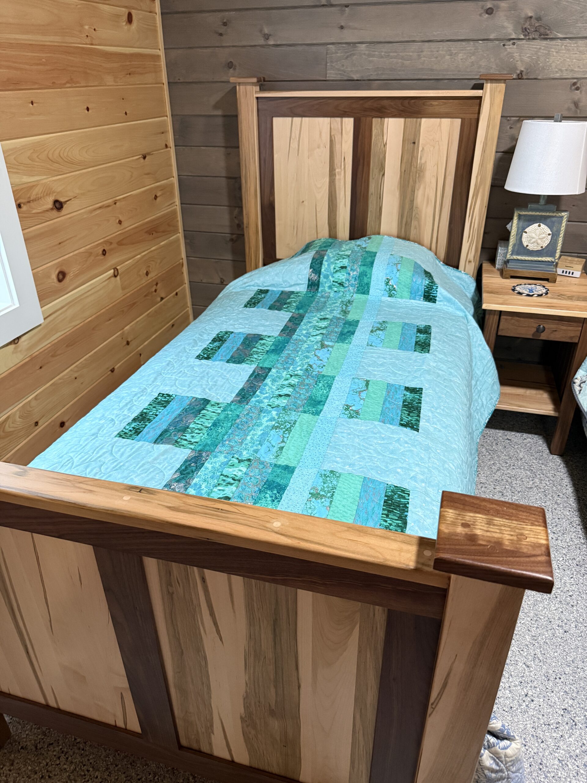 Modern throw quilt featuring vertical strips of varied teal fabrics against light teal background with all over long arm quilting