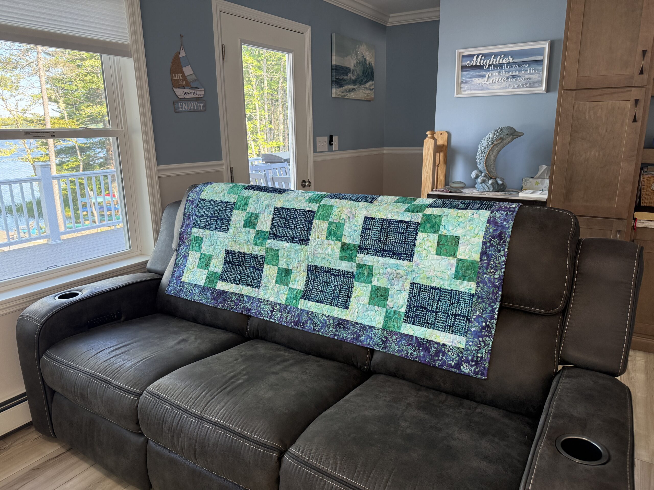 Handmade lap quilt featuring a geometric mosaic of blue and green batik fabrics with a coordinating batik backing.
