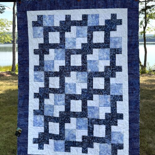 Throw quilt with Wandering Way pattern creating interlocking path in blues and whites with floral backing