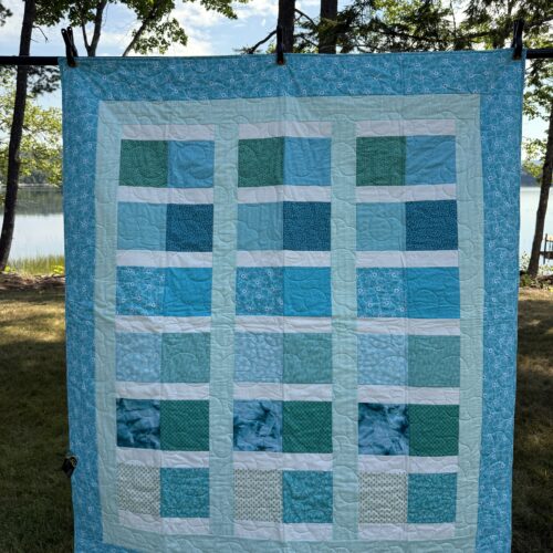 Throw quilt with stacked rectangle blocks in various teal and aqua fabrics separated by white sashing with teal floral border