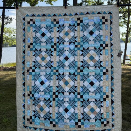 Throw quilt with Turkey Tracks block pattern in beach colors of teal, tan, chocolate, and white with diagonal striped centers and flying geese and tan borders