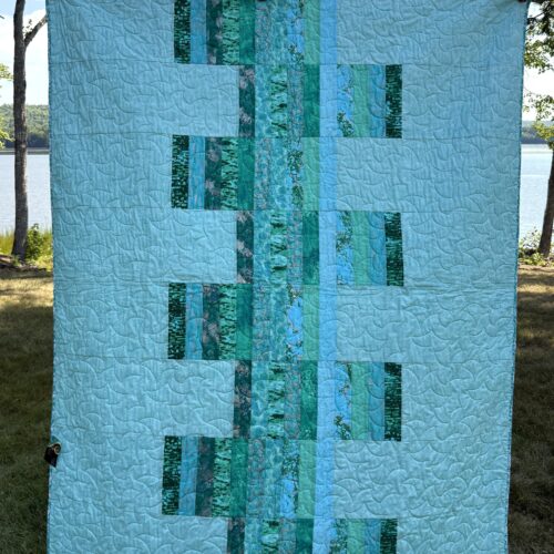 Modern throw quilt featuring vertical strips of varied teal fabrics against light teal background with all over long arm quilting