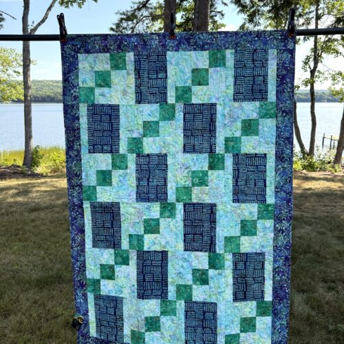 Handmade lap quilt featuring a geometric mosaic of blue and green batik fabrics with a coordinating batik backing.