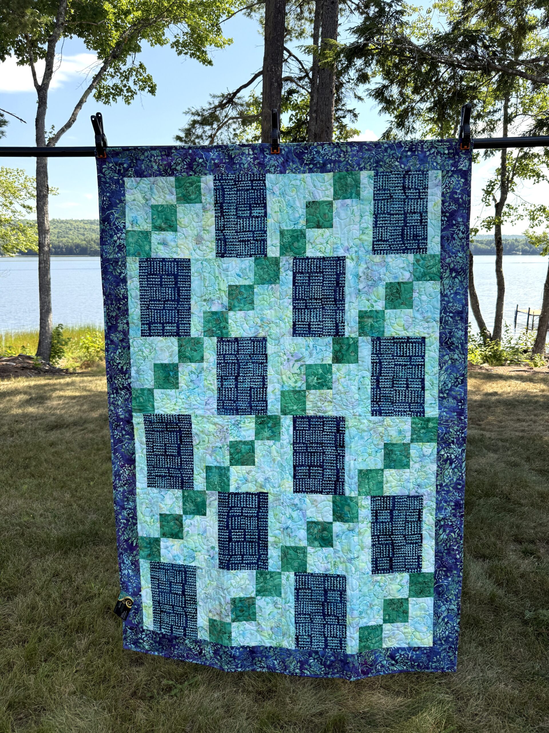 Handmade lap quilt featuring a geometric mosaic of blue and green batik fabrics with a coordinating batik backing.