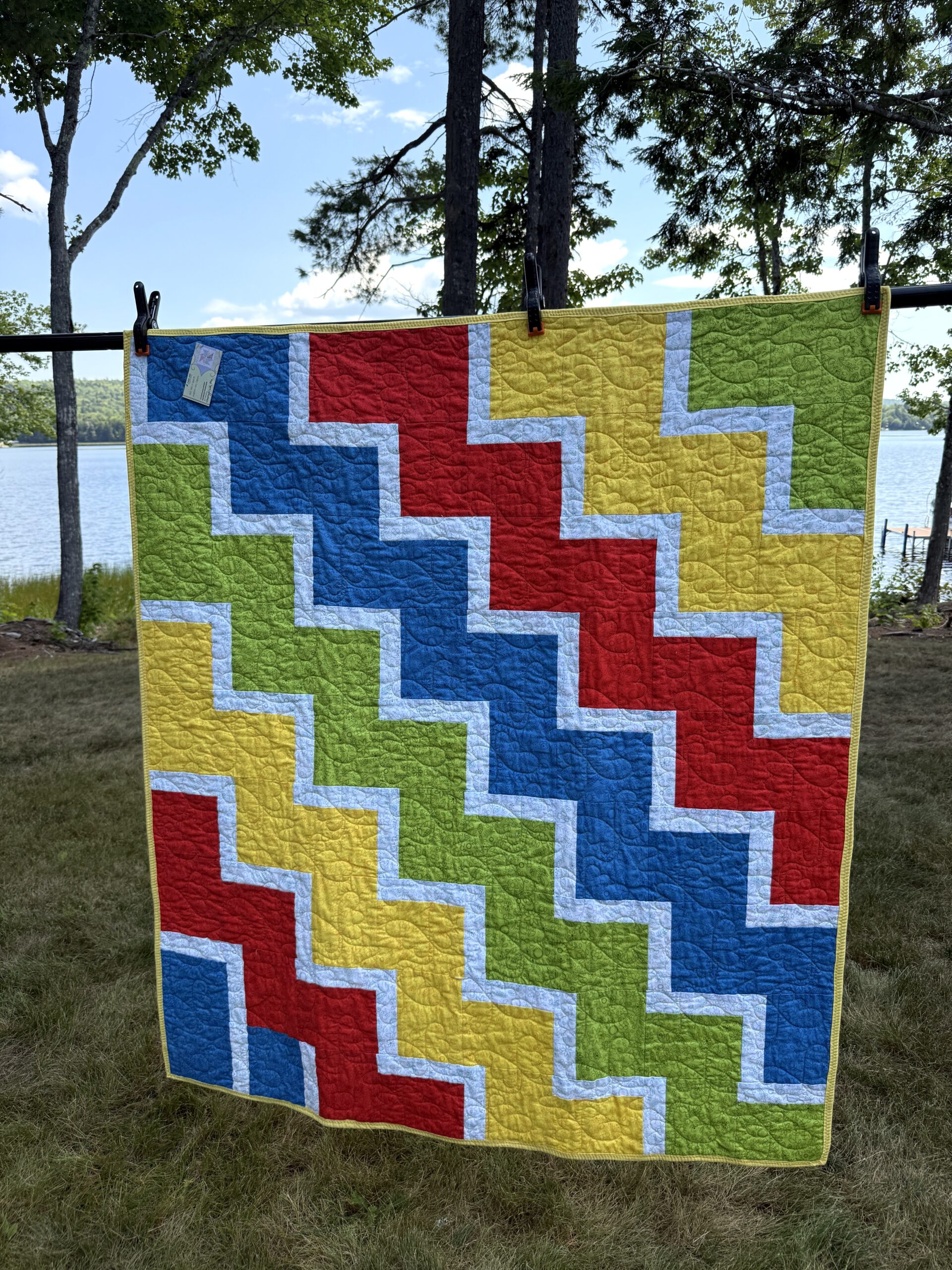 Lap quilt with interlocking zigzag blocks in primary colors red, yellow, blue, and green with white sashing and polka dot backing
