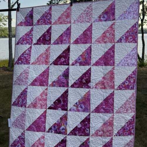 Throw quilt with half square triangles in white and various pink and purple dragonfly and floral prints with dragonfly quilting