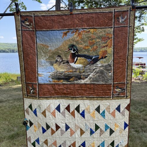 Lap quilt featuring wood duck pair panel in autumn colors with multiple borders and Migrating Geese blocks in earth tones below