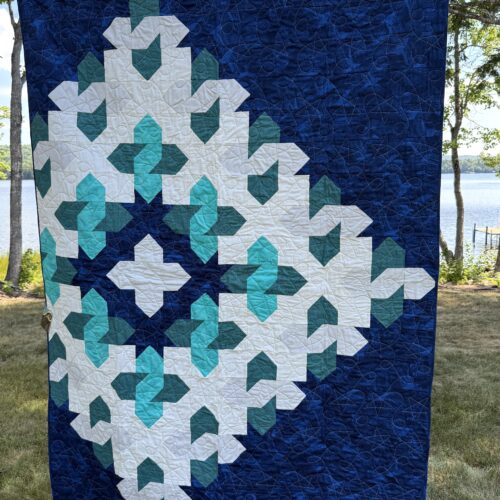 Throw quilt with large geometric star cosmic cloud pattern with teal shades on navy blue background with star and loop quilting motif