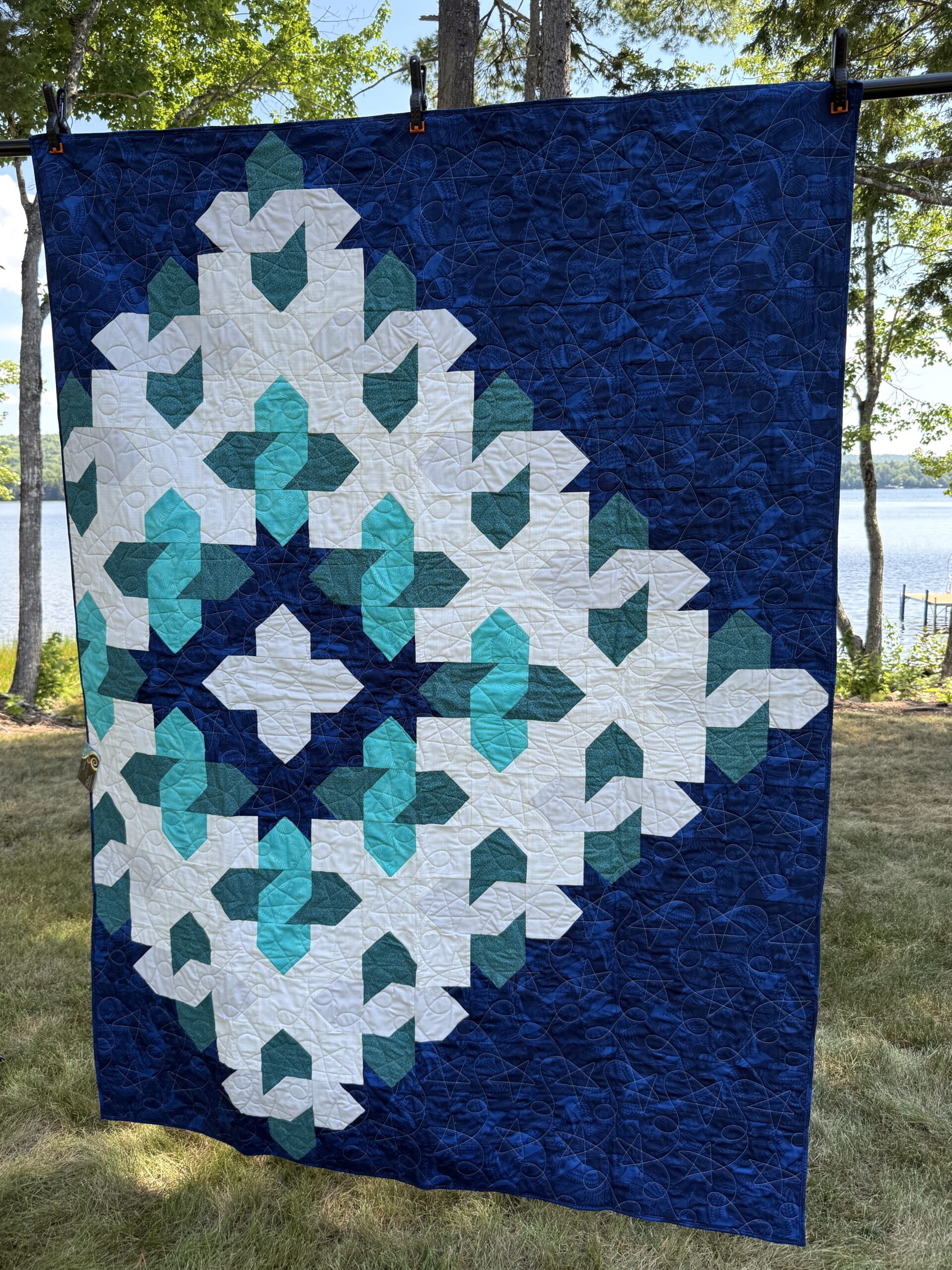 Throw quilt with large geometric star cosmic cloud pattern with teal shades on navy blue background with star and loop quilting motif