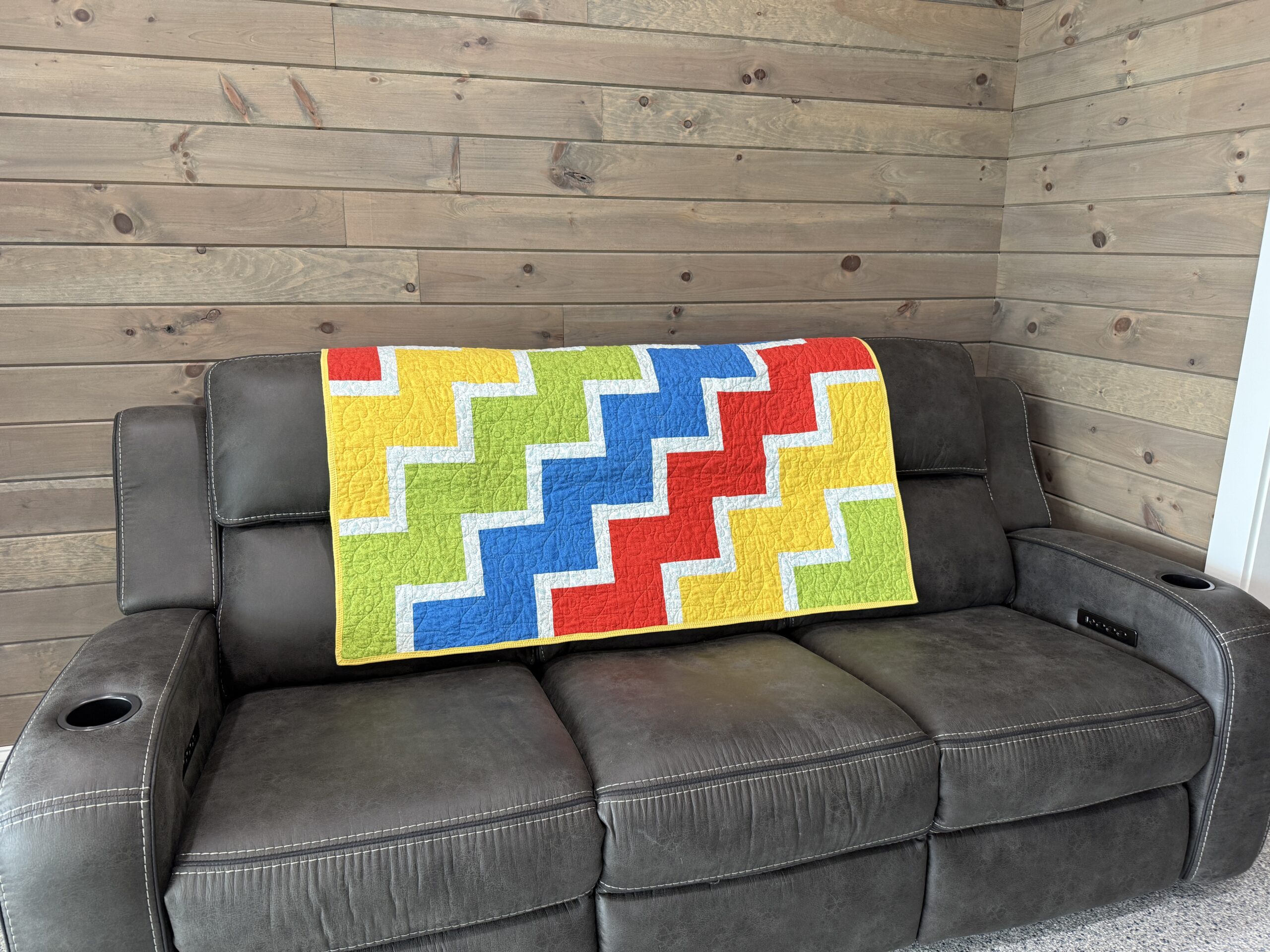Lap quilt with interlocking zigzag blocks in primary colors red, yellow, blue, and green with white sashing and polka dot backing