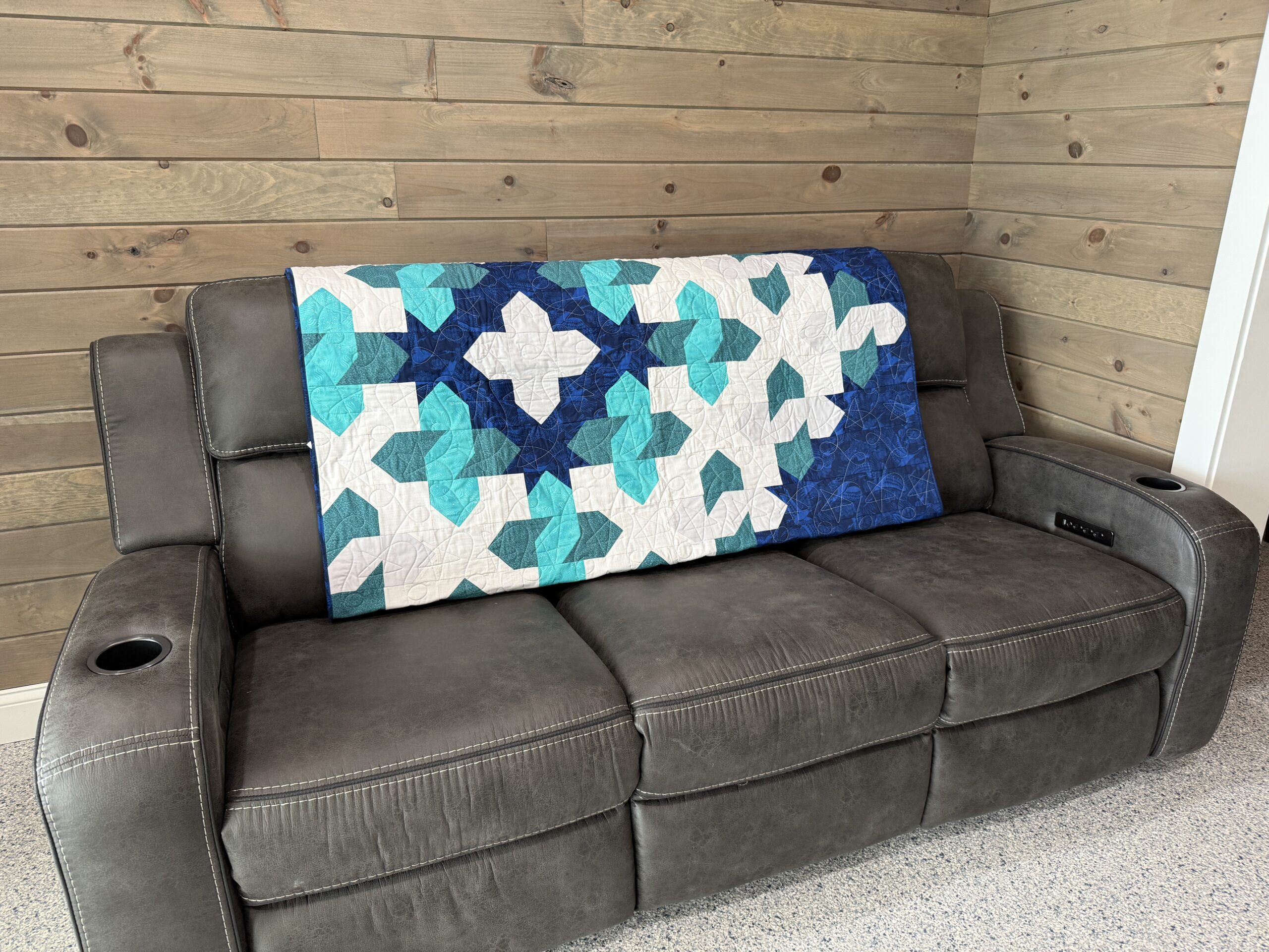 Throw quilt with large geometric star cosmic cloud pattern with teal shades on navy blue background with star and loop quilting motif