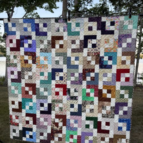 Scrappy throw quilt with light and shadows pattern in many colors with white throughout, creating a geometric pattern