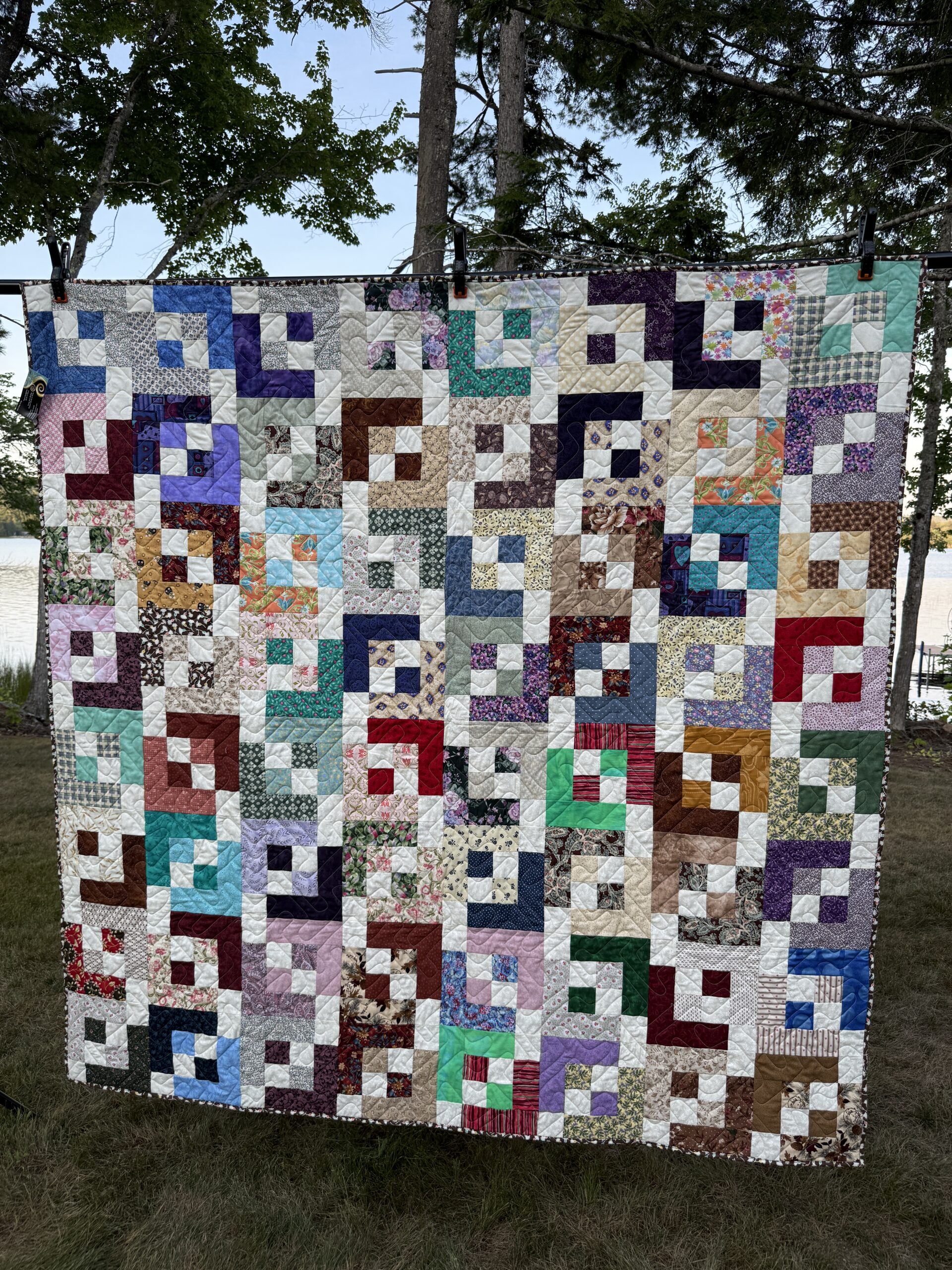 Scrappy throw quilt with light and shadows pattern in many colors with white throughout, creating a geometric pattern