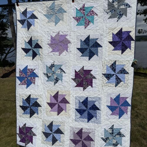 Throw quilt with kindred pinwheel blocks in scrappy blues, purples, teals, and pinks floating on cream background