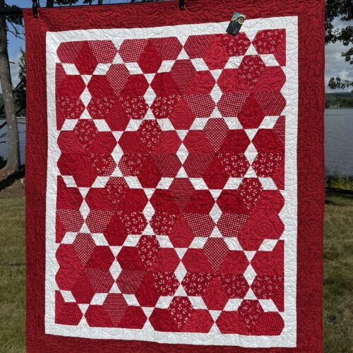Lap quilt with red jewel blocks in various prints separated by white diamonds with red border