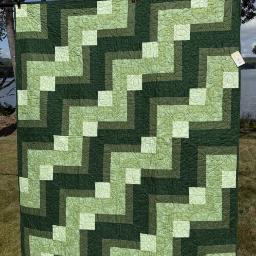 Throw quilt with quarter log cabin blocks in shades of green from forest to light green with loopy quilting