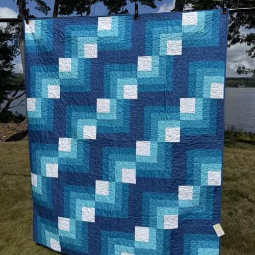 Throw quilt with quarter log cabin blocks in shades of blue with white centers and loopy long arm quilting