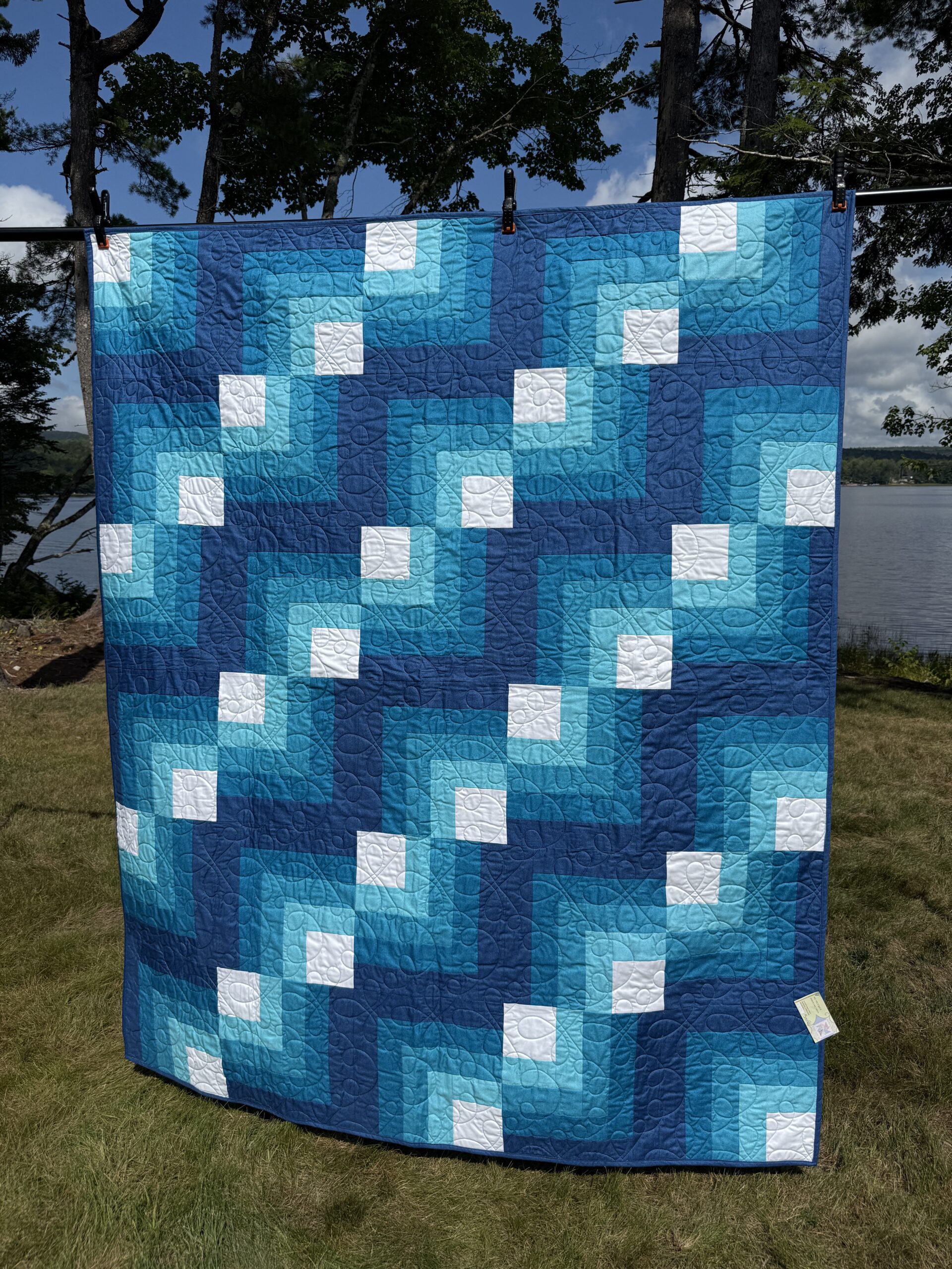 Throw quilt with quarter log cabin blocks in shades of blue with white centers and loopy long arm quilting