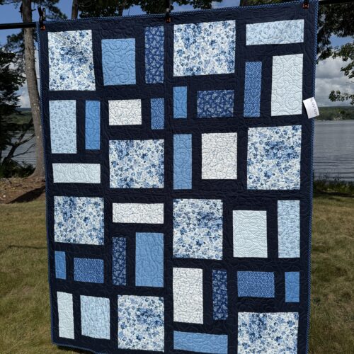 Modern throw quilt with asymmetric rectangular blocks in blue florals, solids, and creams against black sashing