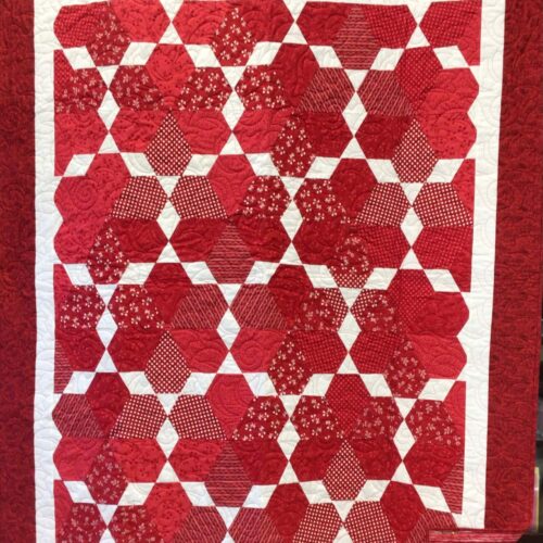 Lap quilt with red jewel blocks in various prints separated by white diamonds with red border