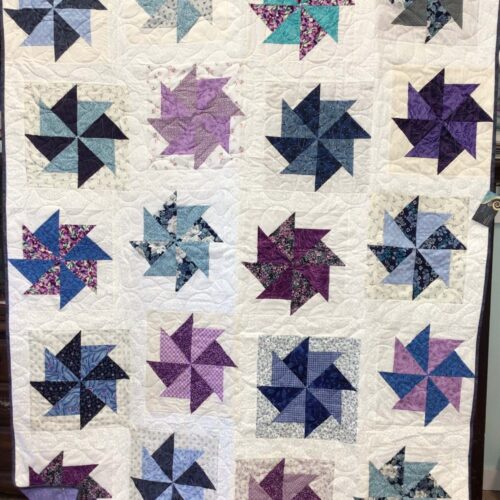 Throw quilt with kindred pinwheel blocks in scrappy blues, purples, teals, and pinks floating on cream background