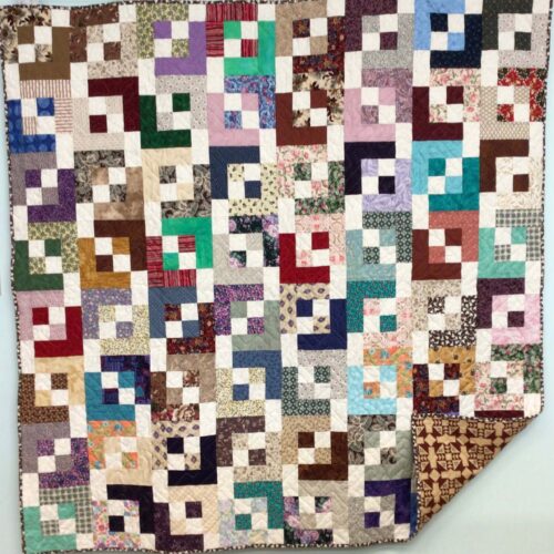 Scrappy throw quilt with light and shadows pattern in many colors with white throughout, creating a geometric pattern