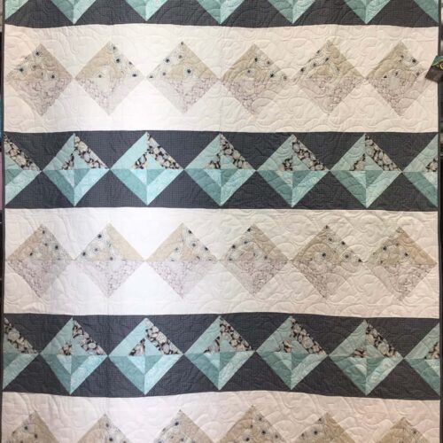 Bed-size quilt with Night and Day blocks set on point creating diamond rows in charcoal gray with teal and cream with neutrals