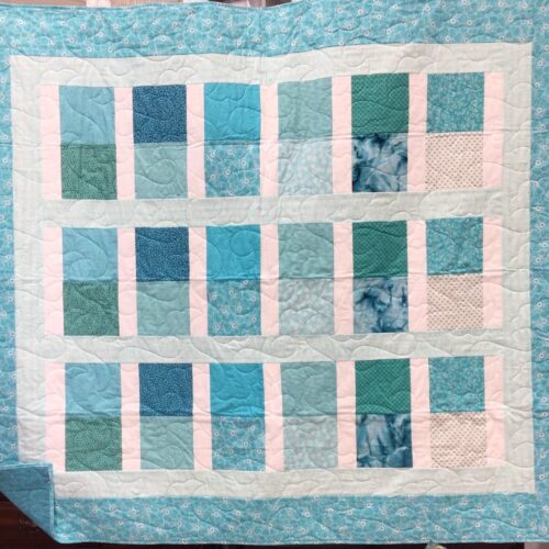 Throw quilt with stacked rectangle blocks in various teal and aqua fabrics separated by white sashing with teal floral border