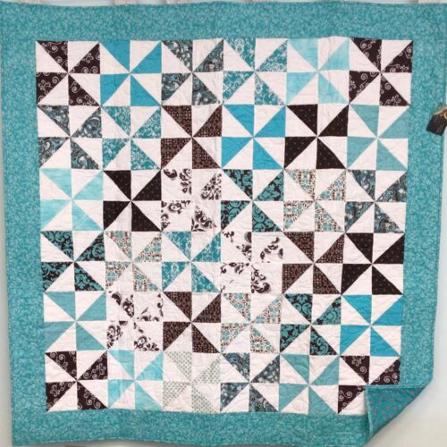 Pinwheel lap quilt in chocolate & teal with mini floral border. Teal backing with pink flowers.