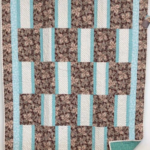 Lap quilt with offset brick pattern featuring brown paisley rectangles alternating with polka dot rectangles, teal sashing, and paisley border