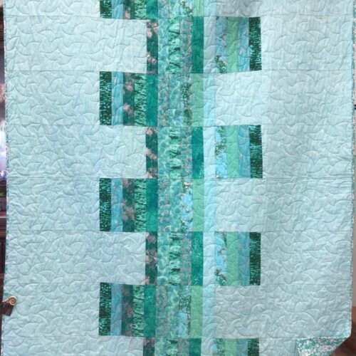 Modern throw quilt featuring vertical strips of varied teal fabrics against light teal background with all over long arm quilting