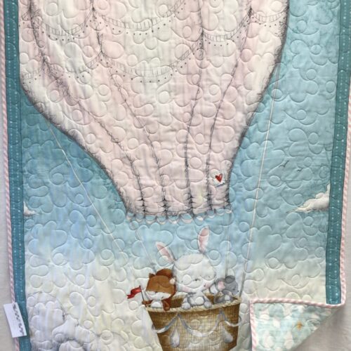 Baby quilt featuring bunny and friends in cream hot air balloon on soft blue sky background with teal borders and long arm quilting
