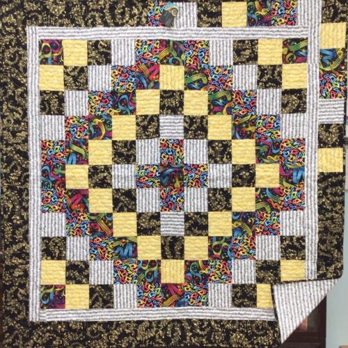 Throw quilt with Trip Around the World pattern featuring small squares in music-themed fabrics radiating from center in concentric rings