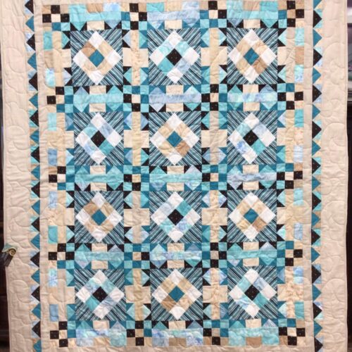 Throw quilt with Turkey Tracks block pattern in beach colors of teal, tan, chocolate, and white with diagonal striped centers and flying geese and tan borders