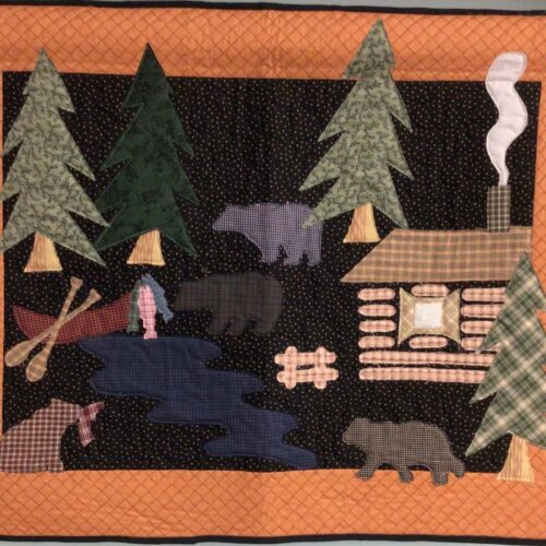 McKenna Ryan Bear Camp quilted wall hanging using raw edge appliqué with rustic plaid fabrics, featuring a log cabin, bears, and a stream.