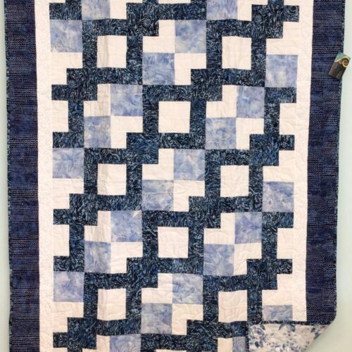 Throw quilt with Wandering Way pattern creating interlocking path in blues and whites with floral backing