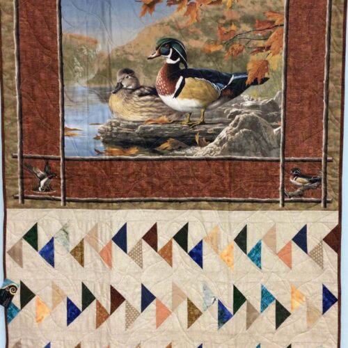 Lap quilt featuring wood duck pair panel in autumn colors with multiple borders and Migrating Geese blocks in earth tones below