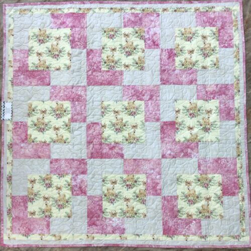 Handmade baby quilt with fawn and floral print blocks framed in rose pink and pale gold, pieced in the Town Square pattern from Fabric Cafe.