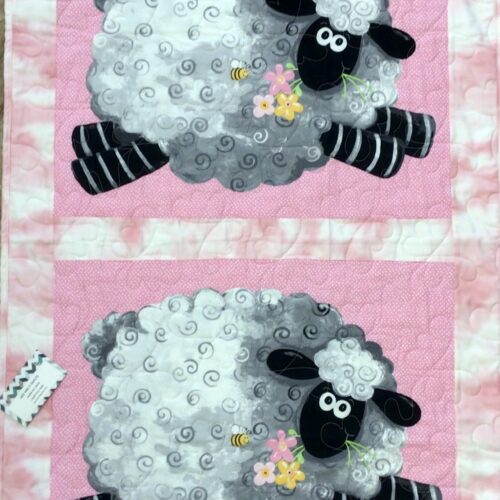Handmade pink baby quilt featuring two large panel-printed cartoon sheep with curly fleece, holding flowers, on a pink polka dot background.