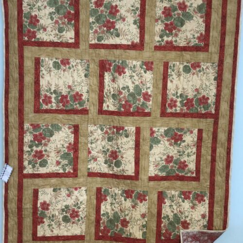 Handmade lap quilt with twelve large red floral print blocks on cream, framed in dark red and gold sashing, pieced in the Bold Blocks pattern by Fabric Café.