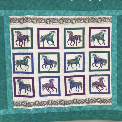 Handmade lap quilt with twelve decorative carousel horses in teal, blue, and purple, framed individually and set against multiple teal borders.